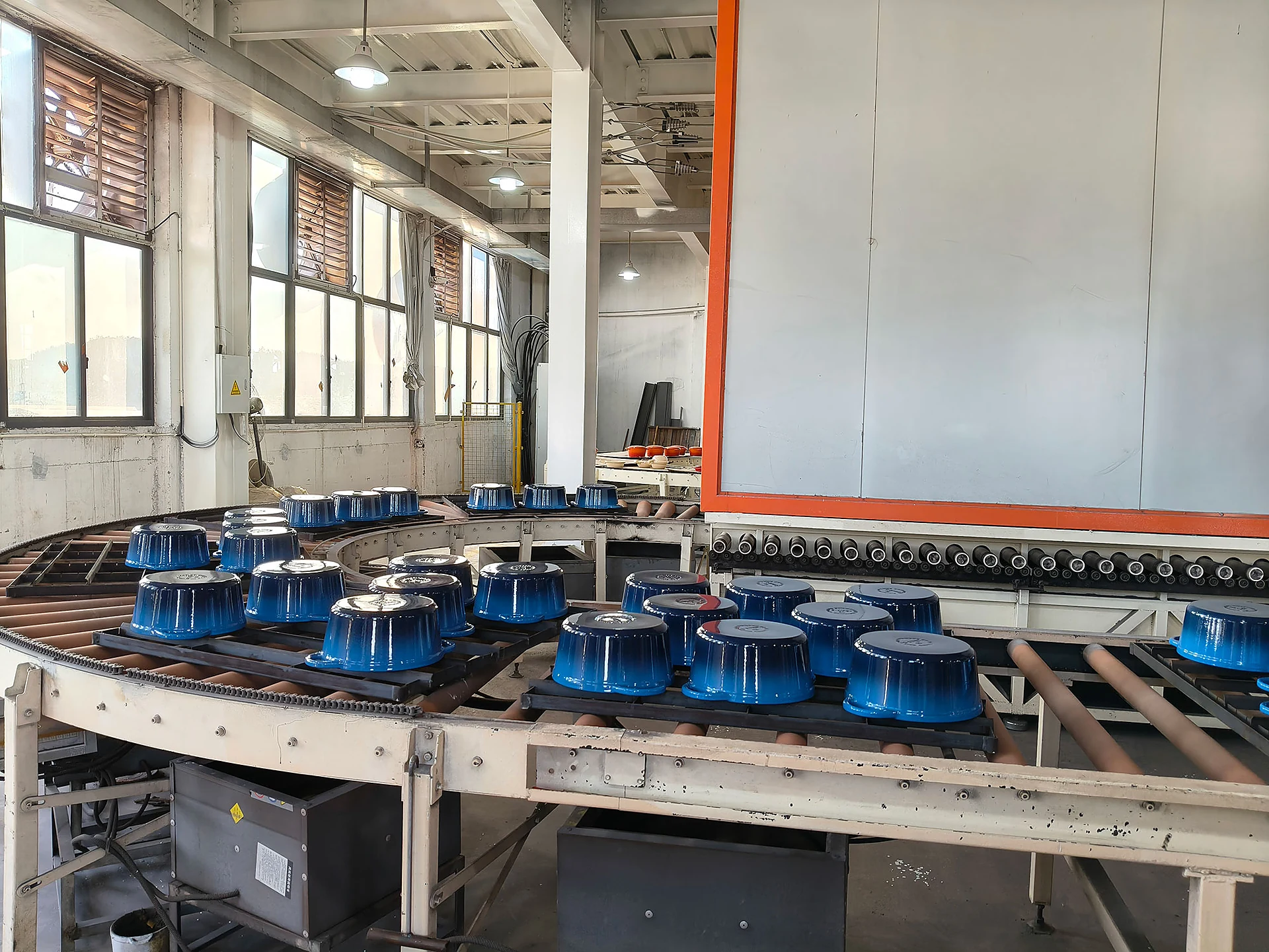 Blue enameled cast iron cookware on conveyor line for quality review